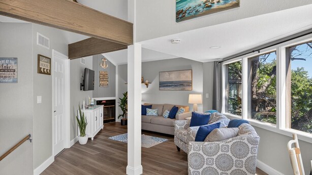 A spacious living room with a large window, a fireplace, and a sofa with patterned cushions.