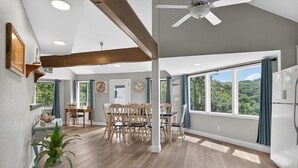 A spacious kitchen with wooden flooring, a dining area with a wooden table and chairs, and large windows offering a view of the outdoors.