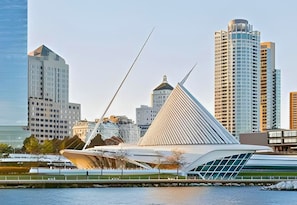 A modern architectural structure with a triangular roof and a glass facade, situated in an urban setting with high-rise buildings in the background.