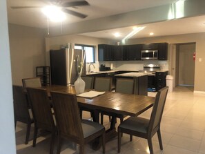 A modern kitchen with dark cabinets, stainless steel appliances, and a dining area with a wooden table and chairs. - Spacious 2300SF, Recently Rehabbed, Large Living (Crosby)