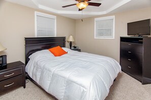 A bedroom with a bed, a nightstand, a lamp, a dresser, a ceiling fan, and a TV.