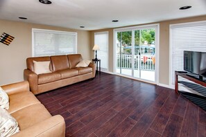 A living room with a brown leather sofa, a TV stand, and a large window with blinds.