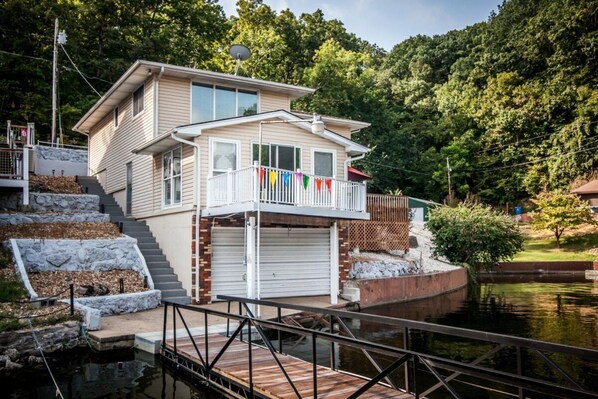 A two-story house with a balcony, a dock, and a stone staircase leading to a garage.