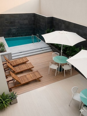 A poolside area with a wooden deck, a pool, and a table with chairs.