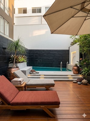 A modern outdoor pool area with lounge chairs, a large umbrella, and a stone wall backdrop. - In the best neighborhood in Barranco, with a view of the ocean. (Cercado de Lima)