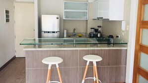 Et moderne køkken med en glasø belagt med to barstole, et køleskab og en kaffemaskine.