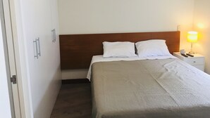Et hotelværelse med en seng, et natbord, en lampe og en dør.