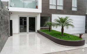 A modern building with a garage door, a stone wall, and a landscaped area with palm trees.