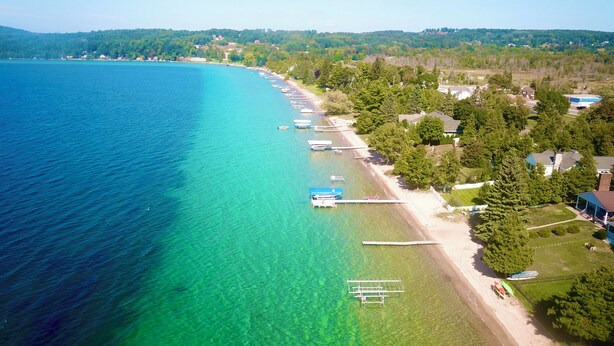 Vue aérienne d’une zone côtière avec des eaux turquoise limpides, une plage de sable et une rangée de bateaux amarrés le long du rivage.
