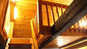 A wooden staircase leading to a lofted area with exposed beams and a sloped ceiling.