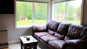 A room with a brown leather sofa, a small wooden table, and a window with a view of houses and trees.