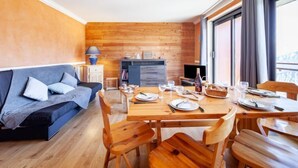 Een moderne kamer met een houten vloer, een bank, een eettafel voor vier personen en een keuken in de achtergrond.