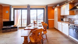 Een moderne keuken met houten kasten, een eettafel met stoelen, een televisie en uitzicht op bergen door grote ramen.