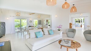 A spacious living area with a white sofa, a round coffee table, and a dining area with a white table and chairs.