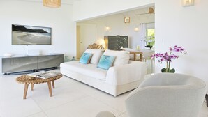 A modern living room with a white sofa, a flat-screen TV, a coffee table, and a chair.