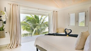 A bedroom with a large bed, a view of palm trees, and a balcony with curtains.