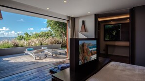 A modern hotel room with a large window, a flat-screen TV, a bed, and a small seating area with a table and chairs. - Villa Blue Swan | Ocean View - Located in  Exquisite Lurin with Private Pool (Lurin)