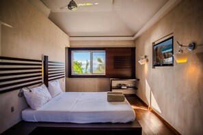 A modern bedroom with a large bed, a TV mounted on the wall, a window with a view of palm trees, and a ceiling fan. - Villa Blue Swan | Ocean View - Located in  Exquisite Lurin with Private Pool (Lurin)