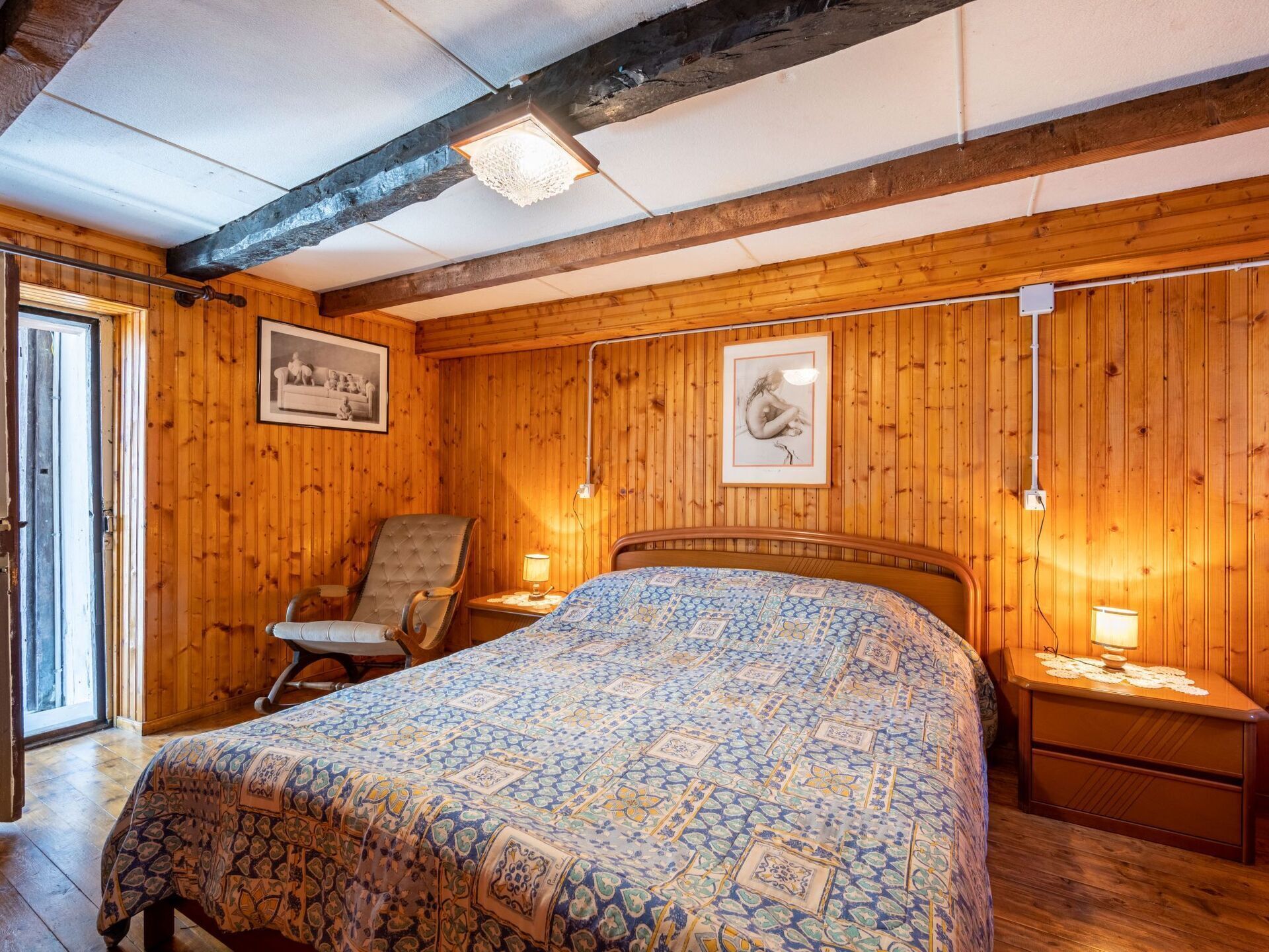 Une chambre à coucher aux murs lambrissés, avec un lit, une chaise, une table de chevet et un tableau encadré accroché au mur.