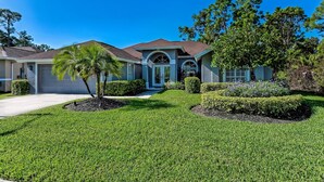 A residential house with a well-maintained lawn, a palm tree, and a driveway leading to a garage. - Naples- Briarwood Estates all new 4BR/3 BA, sleeps 10, vacation rental (Naples)