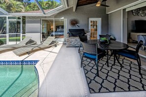 Relax in the covered patio with a dining table and lounge chairs, overlooking the pool.