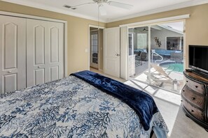 Quarto com cama, penteadeira, televisão e porta de vidro corria para uma varanda com mobiliário de exterior.