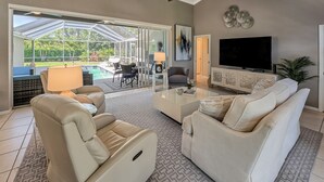 A spacious living room with a large TV, comfortable seating, and a patio area with outdoor furniture. - Naples- Briarwood Estates all new 4BR/3 BA, sleeps 10, vacation rental (Naples)