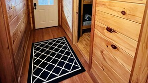 Een houten gang met een geometrisch vloerkleed, een deur met een raam en een groot ‘N’ bord aan de muur.