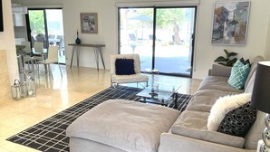 A modern living room with a sofa, a coffee table, and a dining area with chairs and a table. - Gorgeous getaway near El Paseo!  Huge property with huge pool. Tesla charger! (Palm Desert)