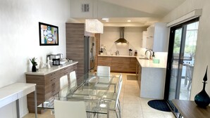 A modern kitchen with a glass dining table, white chairs, and stainless steel appliances. - Gorgeous getaway near El Paseo!  Huge property with huge pool. Tesla charger! (Palm Desert)