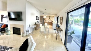 A modern living room with a fireplace, a dining area, and a kitchen. - Gorgeous getaway near El Paseo!  Huge property with huge pool. Tesla charger! (Palm Desert)