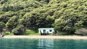 A house by a clear blue lake surrounded by dense green forest.