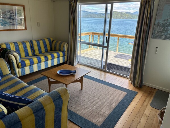 En stue med en stribet sofa, et sofabord og udsigt til en sø gennem en skydedør.