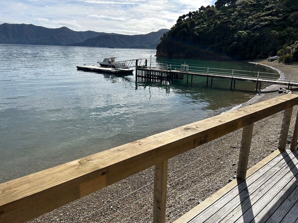 A wooden dock extending into a calm lake with a boat moored at the end. - Sunset Cottage right on the beach. (Marlborough)