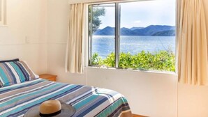 A room with a bed, a window with curtains, and a view of a lake and mountains.