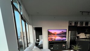Een moderne woonkamer met een grote hoekbank, een flatscreen televisie en een keukenhoek met een koelkast en een magnetron.