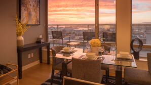 Een eetgedeelte met een glazen tafel, stoelen en een uitzicht op een zonsondergang boven een stadsbeeld.