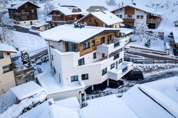A multi-story building with balconies, a parking area, and snow-covered surroundings.