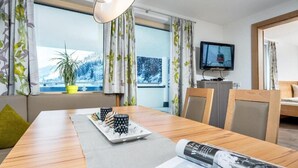 Ein modernes Hotelzimmer mit einem Holztisch, einem an der Wand befestigten Fernseher und Blick auf verschneite Berge durch die Fenster.
