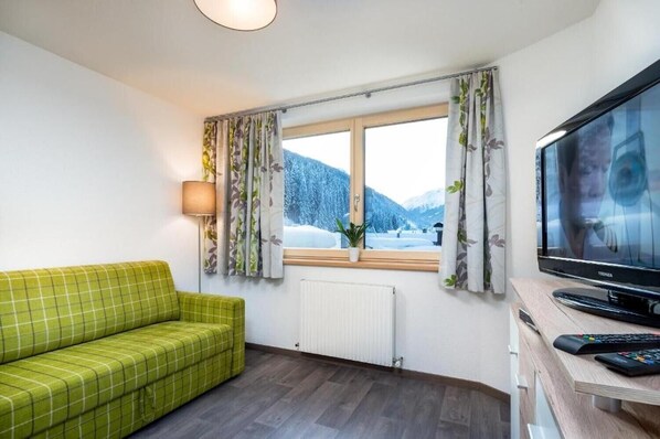 Een kamer met een groene bank, een televisie, een raam met gordijnen en een radiator.