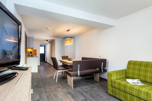 Ein modernes Hotelzimmer mit Fernseher, einer Essecke mit Tisch und Stühlen, einer Couch und einer Pendelleuchte.