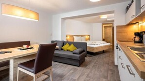 Una habitación de hotel moderna con comedor, sofá con cojines, cama y cocina.