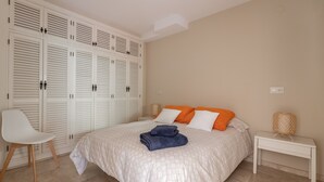 A bedroom with a bed, white wardrobe, white nightstand, and a chair. - "Los Girasoles" Apartment with Sea View, Wi-Fi, and Terrace (La Herradura)