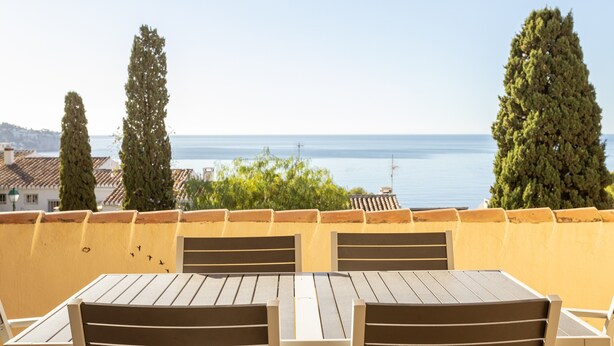 A terrace with a table and chairs, overlooking a body of water and greenery. - "Los Girasoles" Apartment with Sea View, Wi-Fi, and Terrace (La Herradura)