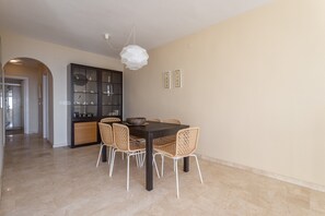 Un comedor con una mesa de madera oscura, sillas de mimbre, una lámpara colgante blanca y un aparador de vidrio con adornos.