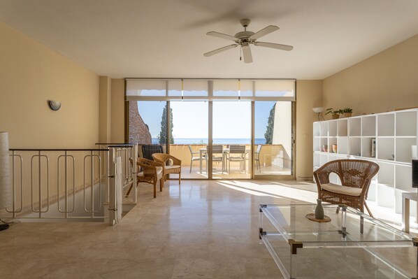 Una habitación amplia con balcón, ventilador de techo y un gran ventanal con vistas al mar.