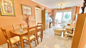 A dining area with a table and chairs, a kitchen in the background, and a living area with a sofa and a coffee table. - "Oasis" Apartment near the Beach with Sea View, Pool, Wi-Fi, and Terrace (La Herradura)