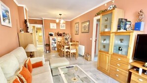 A living room with a sofa, ottoman, glass coffee table, wooden cabinet, and a television. - "Oasis" Apartment near the Beach with Sea View, Pool, Wi-Fi, and Terrace (La Herradura)
