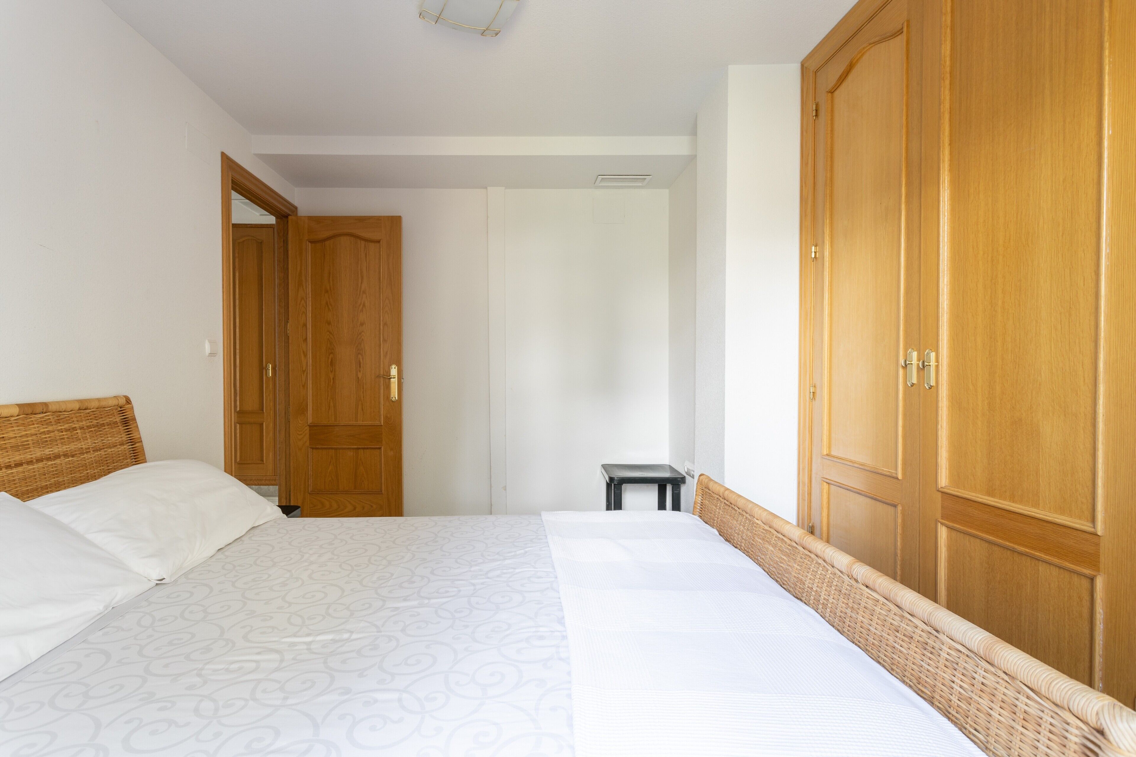 A bedroom with a bed, wooden wardrobe, and a small table.