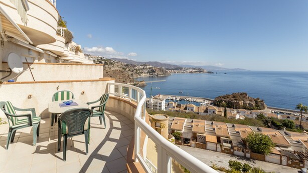 A balcony with a table and chairs overlooking a coastal town and the sea. - Apartment "Brisa de mar" Near the Beach with Sea View, Pool & Terrace (La Herradura)